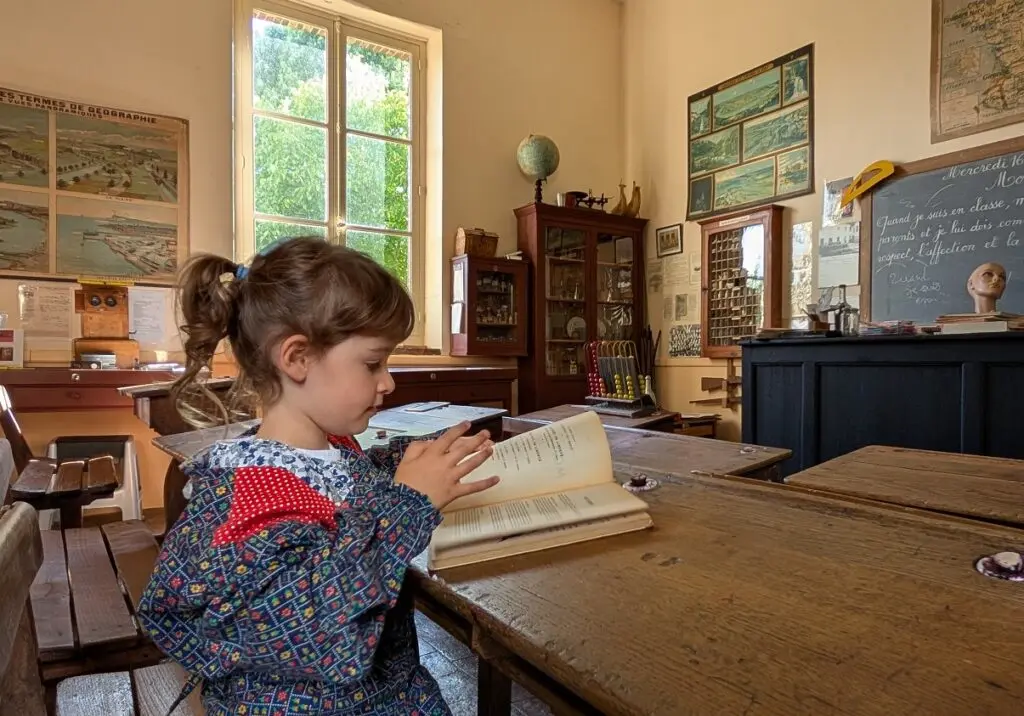 Petite fille en blouse d’école avec un livre au Musée école d’Unverre